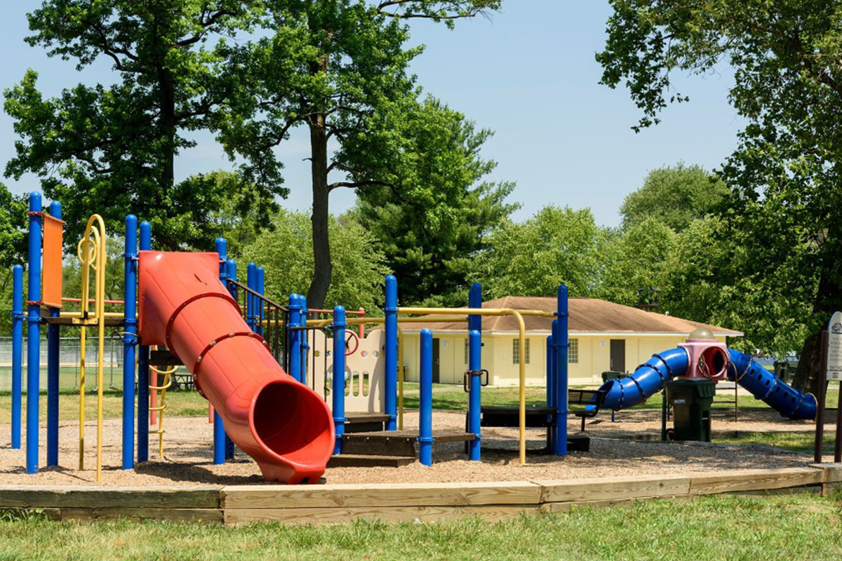 A colorful outdoor playground with a red slide. In the background is a single-story yellow building.