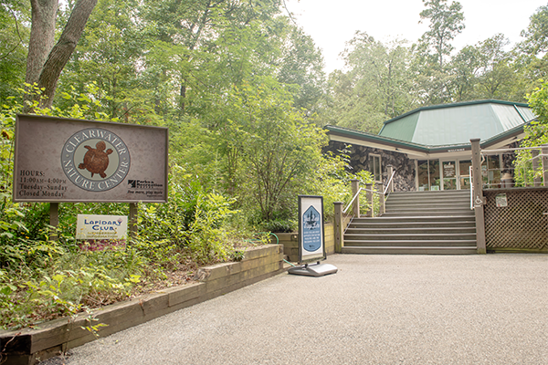A pathway with stairs leading to a building, surrounded by forest. A wooden sign reads CLEARWATER NATURE CENTER.