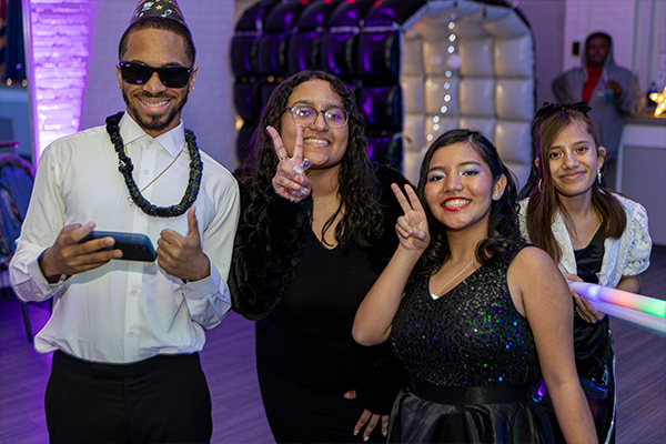 four teens standing and posing for the camera. They are wearing black and white attire at a colorful dance venue.
