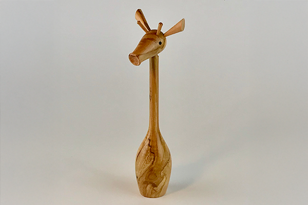 A minimalist wooden sculpture of a stylized giraffe against a grey background.