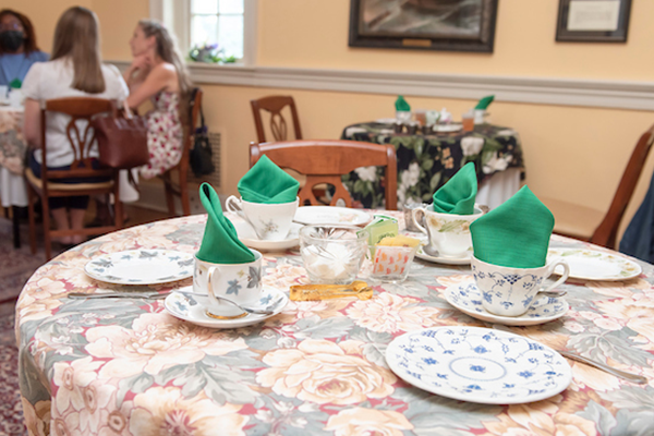 A table for four nicely decorated with plates and cups, in a yellow room with a chair rail. There are green napkins folded and rising out of the tea cups.