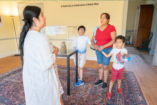 A guide speaks to visitors in a historic room near a glass case containing several artifacts.