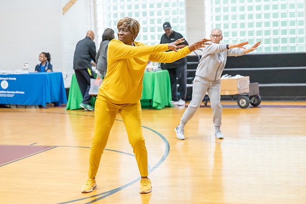 Two adults in comfortable clothes do aerobics in a gym.