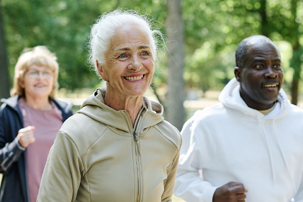 Three smiling seniors wearing exercise clothing near a wooded area.