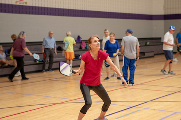 Seniors play pickleball in a gym.