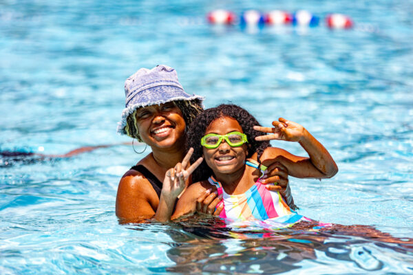 A woman holding a small girl pose for the camera in an outdoor pool.