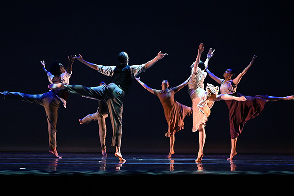 Six dancers perform arabesques in a circle onstage.