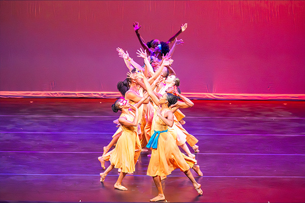 A dance troupe in matching yellow costumes performs on a stage.
