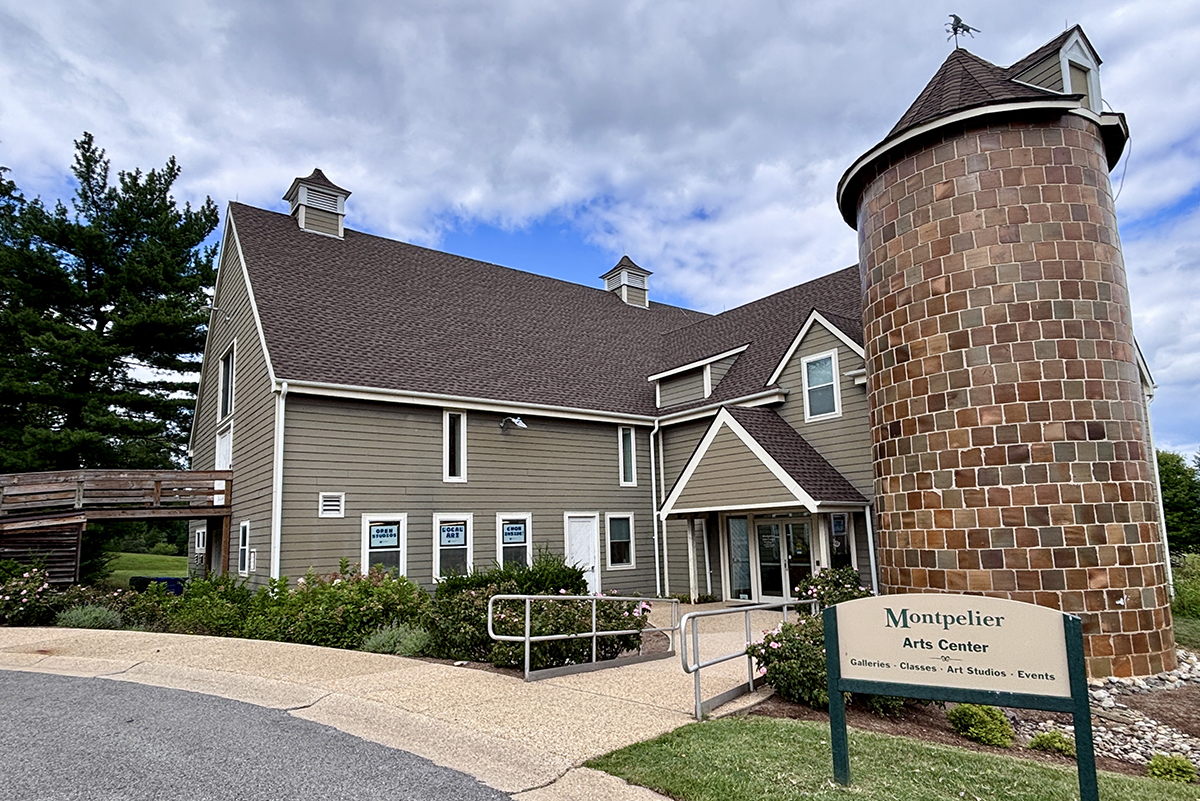 A barn-like, two-story building with a masonry silo tower and multiple windows. A sign in front reads Montpelier Arts Center - Galleries - Classes - Art Studios - Events.