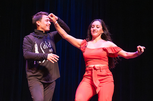 A man and woman dancing together on stage in matching red and black Latin dance outfits.