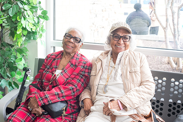 Two smiling seniors share a bench near a sunny window.
